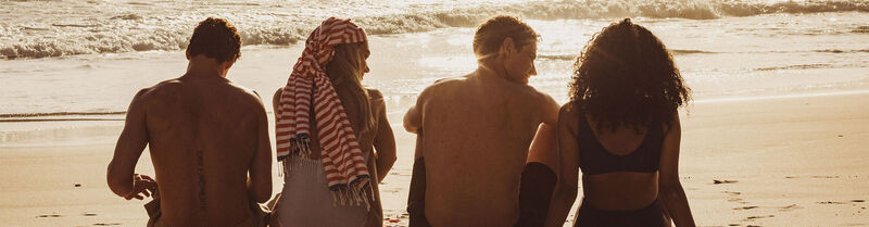 Vier Freunde sitzen in Badesachen am sonnigen Sandstrand