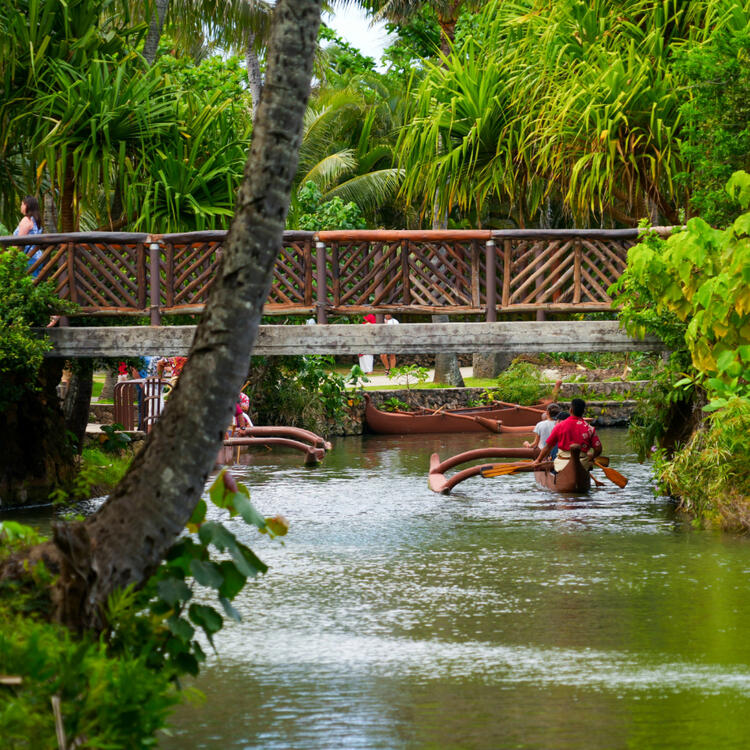 Traditionelle polynesische Kanufahrt auf einem ruhigen Fluss unter einer Brücke, umgeben von üppigem Grün in Hawaii
