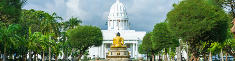 Goldene Buddha-Statue vor dem weißen Rathaus in Colombo, Sri Lanka, umgeben von Palmen und einem reflektierenden Wasserbecken.