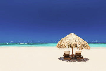 Zwei Liegestühle unter einem Strohsonnenschirm am Strand von Punta Cana, im Hintergrund das Meer