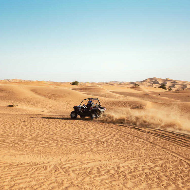 Fahrt im Geländewagen durch die Sanddünen während einer Wüstensafari in Dubai, mit goldenem Sand in der Ferne unter einem klaren blauen Himmel.