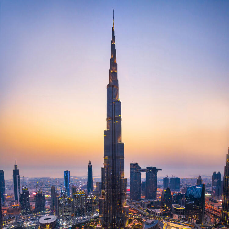 Burj Khalifa bei Sonnenuntergang in Dubai, VAE, mit beleuchteter Stadtlandschaft im Vordergrund