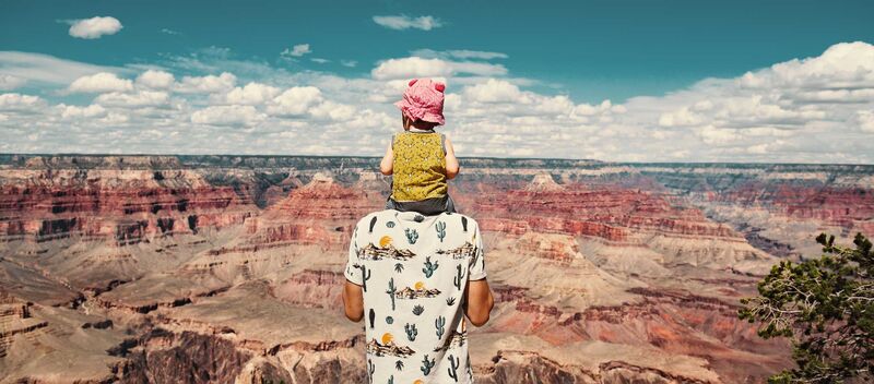 Ein Mann steht über dem Grand Canyon, sein kleines Kind hat er auf den Schultern