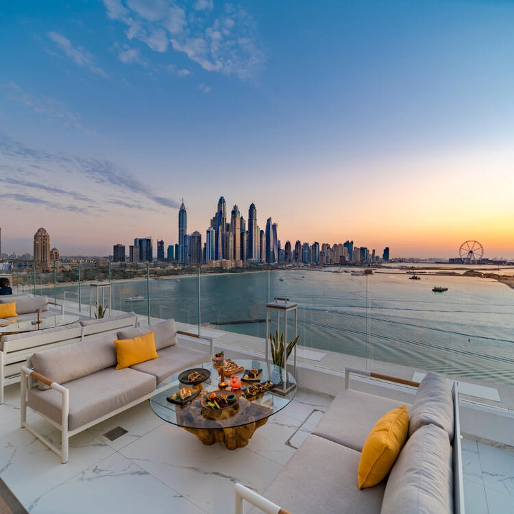 Palm Jumeirah Aufnahme des Palm Jumeirah, umgeben von blauem Wasser, mit der Skyline der Stadt im Hintergrund unter einem klaren blauen Himmel.