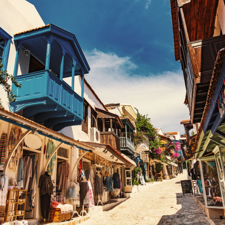 Malerische Einkaufsstraße in einer türkischen Stadt mit traditionellen Gebäuden, farbenfrohen Geschäften und blau gestrichenen Balkonen unter strahlendem Himmel.