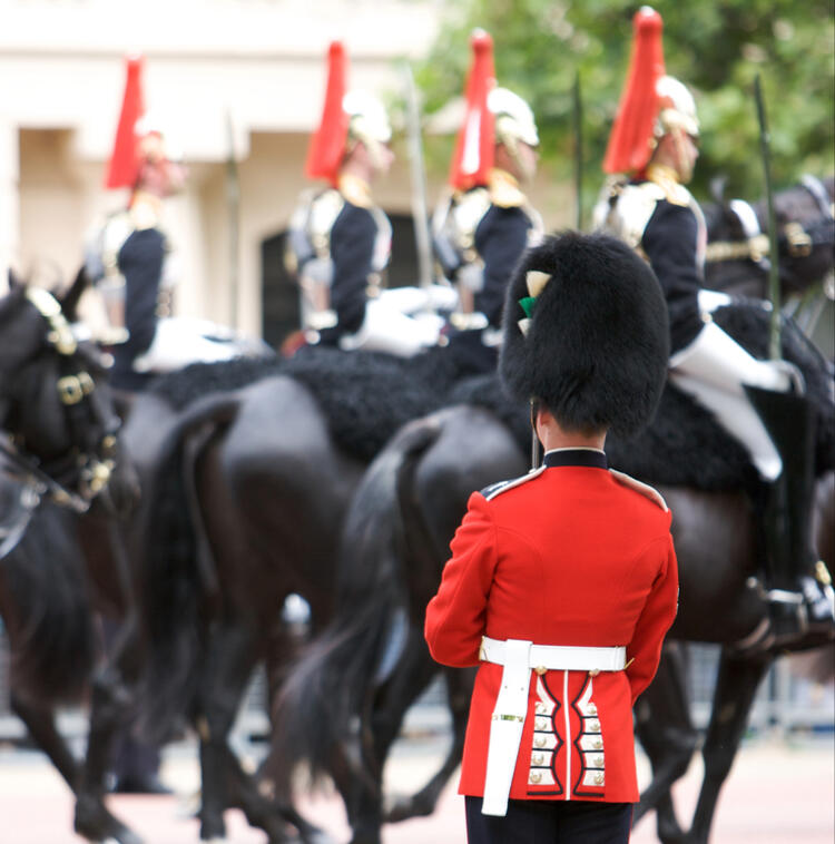 Gardewechsel am Buckingham Palace London Britischer Gardesoldat in roter Uniform beobachtet den Vorbeimarsch berittener Soldaten auf schwarzen Pferden.