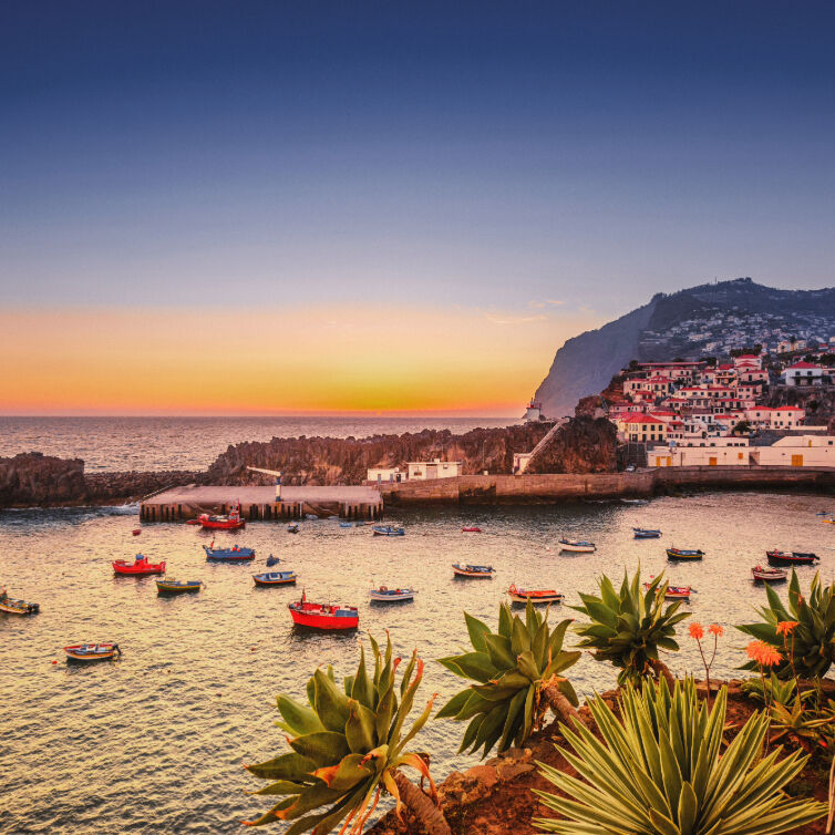 Sonnenuntergang über einer Bucht auf Madeira mit bunten Fischerbooten und Küstenhäusern.