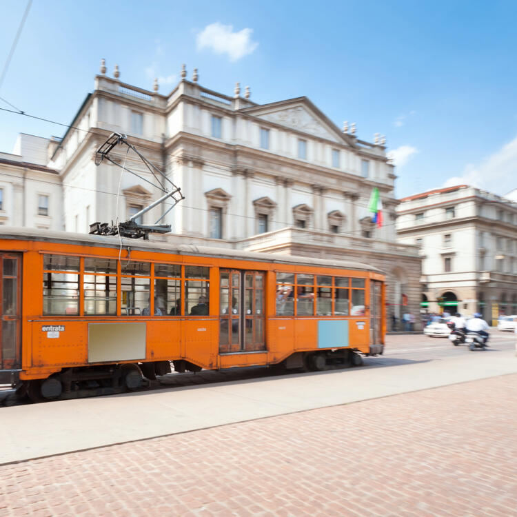 Teatro alla Scala, Mailand, Italien Ansicht des Theaters in Mailand mit einer orangefarbenen Straßenbahn im Vordergrund und blauem Himmel