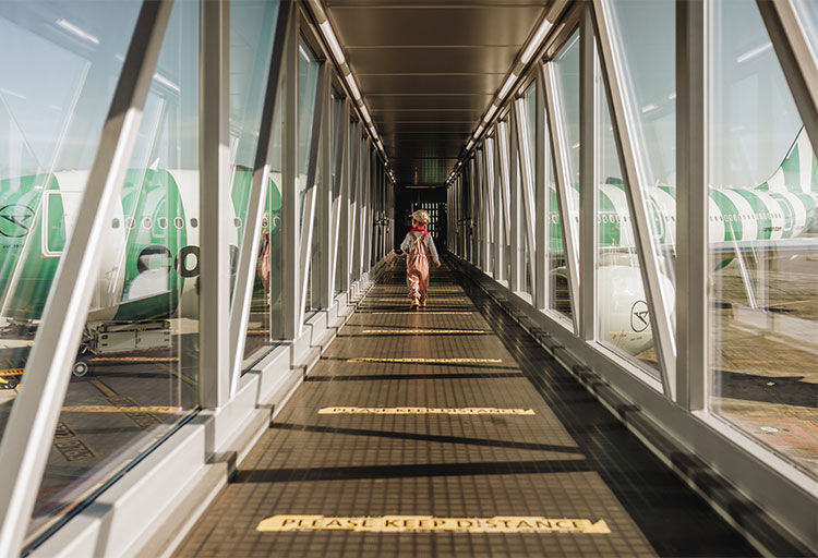 Ein kleiner Junge läuft über die Passagierbrücke zum Einsteigen in ein grün-weiß gestreiftes Condor Flugzeug