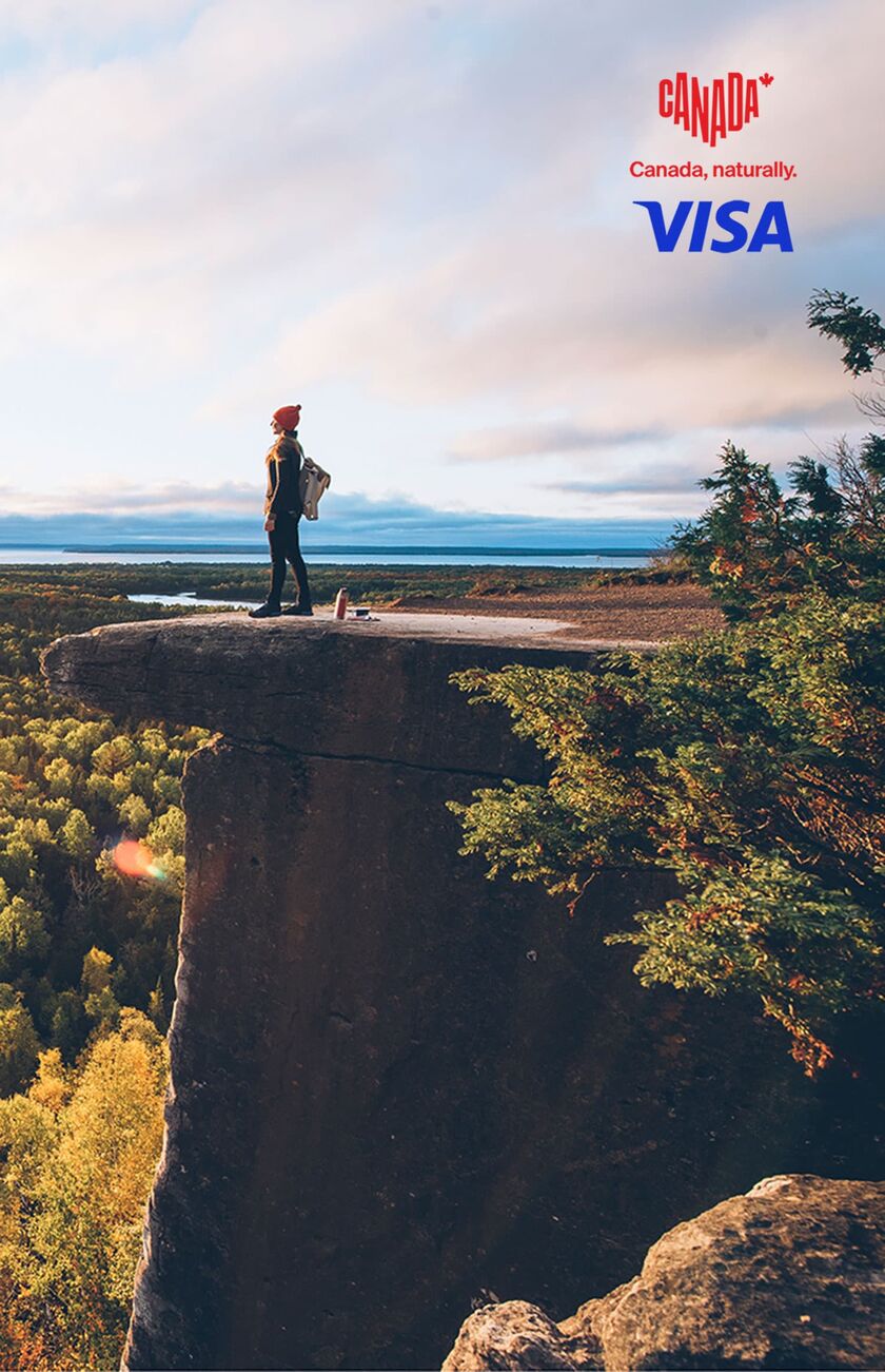 mit Visa 20 % auf Flüge nach Kanada sparen Frau steht auf einem Fels und schaut die Natur Ontarios an.