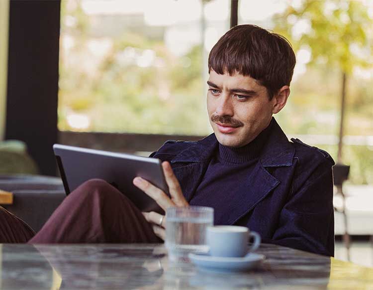 Ein Mann sitzt an einem Tisch und checkt sich über Tablet online für seinen Flug ein
