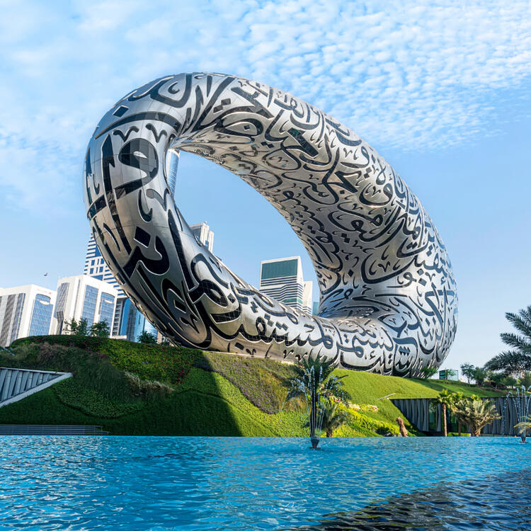 Das Museum der Zukunft in Dubai mit seiner charakteristischen ovalen Struktur, die mit arabischen Kalligraphien verziert ist, mit modernen Wolkenkratzern im Hintergrund und einem reflektierenden Pool im Vordergrund.