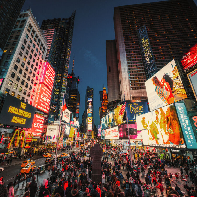 Menschenmengen am belebten Times Square in New York City bei Nacht, umgeben von leuchtenden Werbetafeln und hohen Gebäuden.