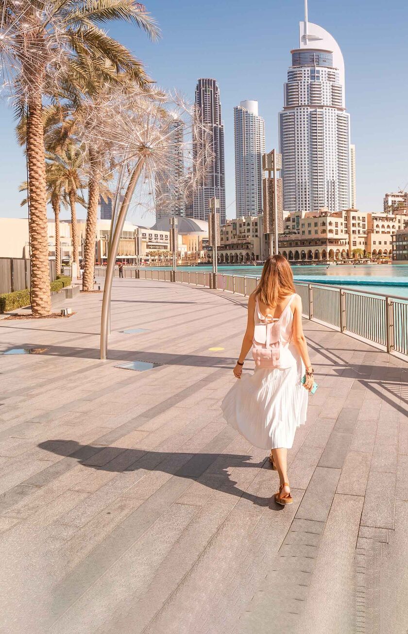 Dubai Eine Frau läuft am Wasser in Dubai entlang auf die Stadt zu