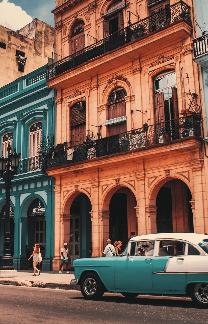 Un coche antiguo de color turquesa frente a una colorida hilera de casas en La Habana.