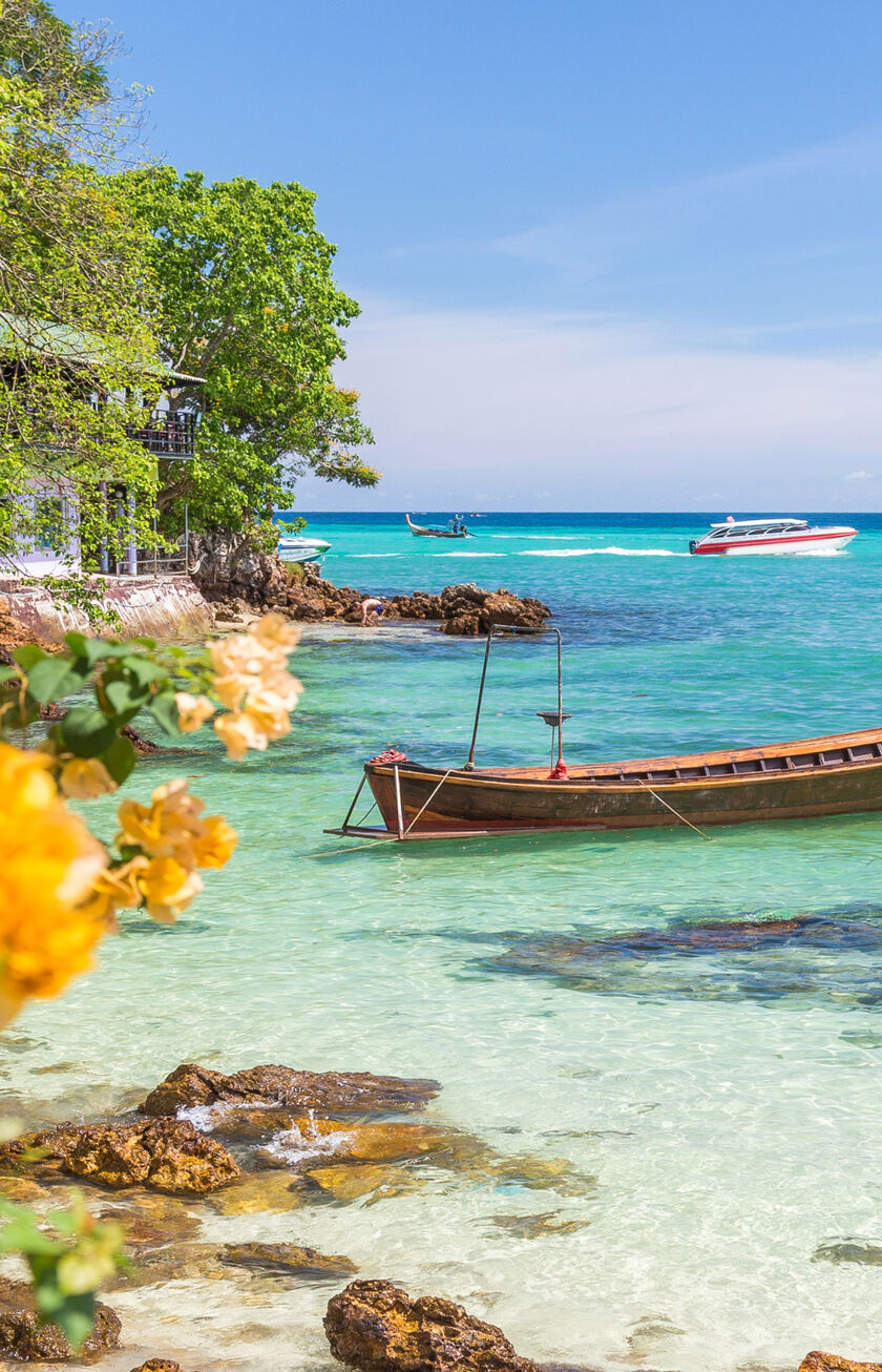 A traditional wooden boat is moored in crystal-clear water in front of a tropical island