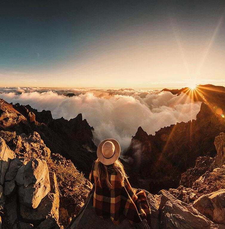 A woman is standing on a mountain in Teneriffa at sunrise, overlooking the clouds