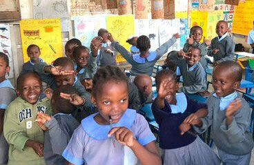 A school class stands in the classroom, dancing, happy and waving at the camera.