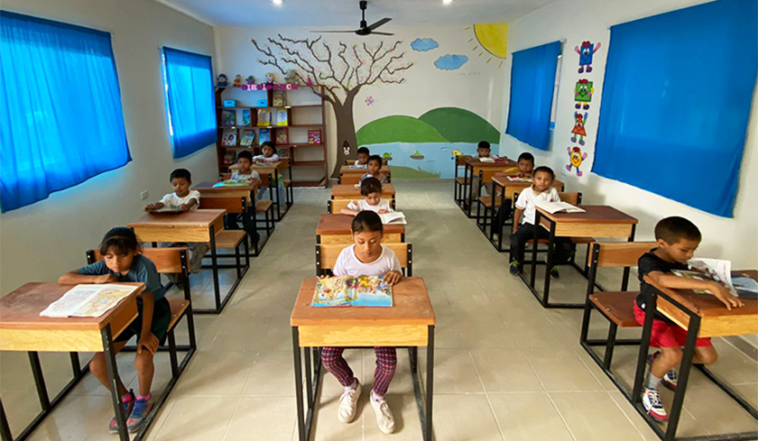 School in Mexico. Children sit at their school desks. The walls are painted with trees. 