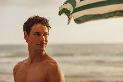 Man on the beach with green striped parasol 