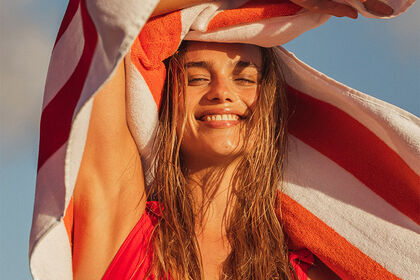 Woman on the beach smiling with red striped towel 