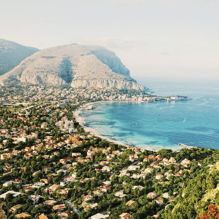 Vista panoramica su Mondello, Palermo: mare cristallino, spiaggia dorata e montagne sullo sfondo.