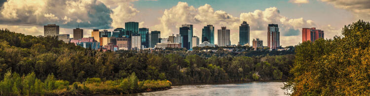 Skyline van Edmonton, Canada, met een rivier op de voorgrond en wolkenkrabbers tegen een bewolkte hemel.