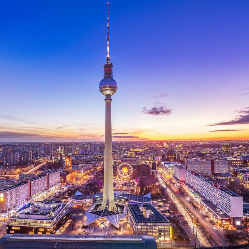 Aerial view of Berlin at sunset, featuring the Berlin TV Tower (Fernsehturm) surrounded by cityscape and vibrant evening colors.