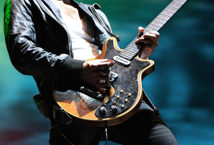 Close-up of hands playing an electric guitar with a blurred green background.